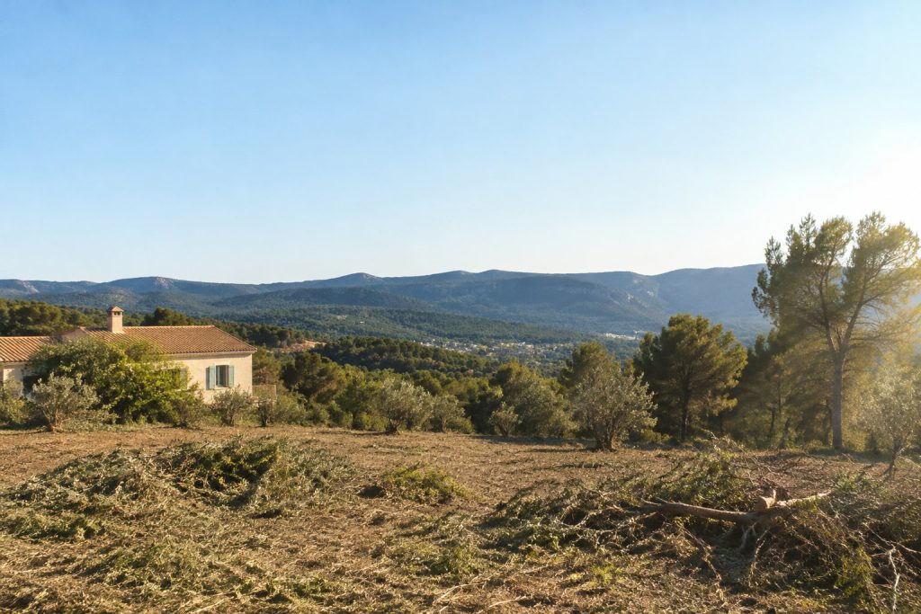 Une maison provençale entourée d'un terrain débroussaillé avec des collines en arrière-plan.